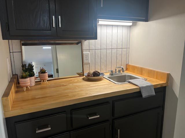 A kitchen with black cabinets , wooden counter tops , a sink and a mirror.