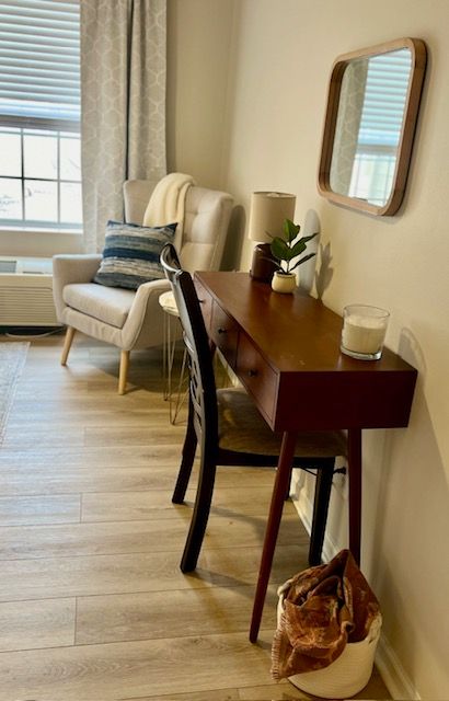 A living room with a desk , chair , and mirror.