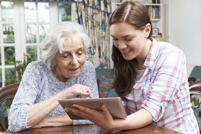 A young woman is helping an older woman use a tablet computer.