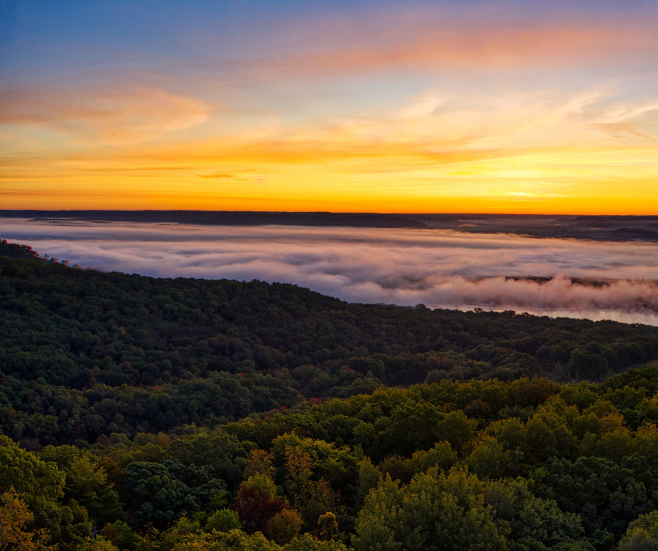 A sunset over a valley with trees and clouds