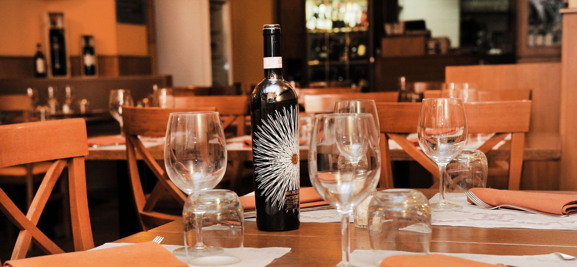 Tavolo del ristorante apparecchiato con bicchieri da vino e una bottiglia, pronto per il servizio.