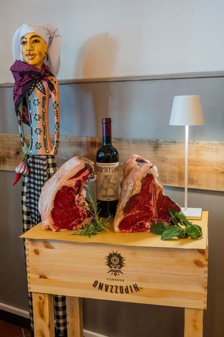 Due bistecche crude, una bottiglia di vino e una figura decorativa su una scatola di legno.