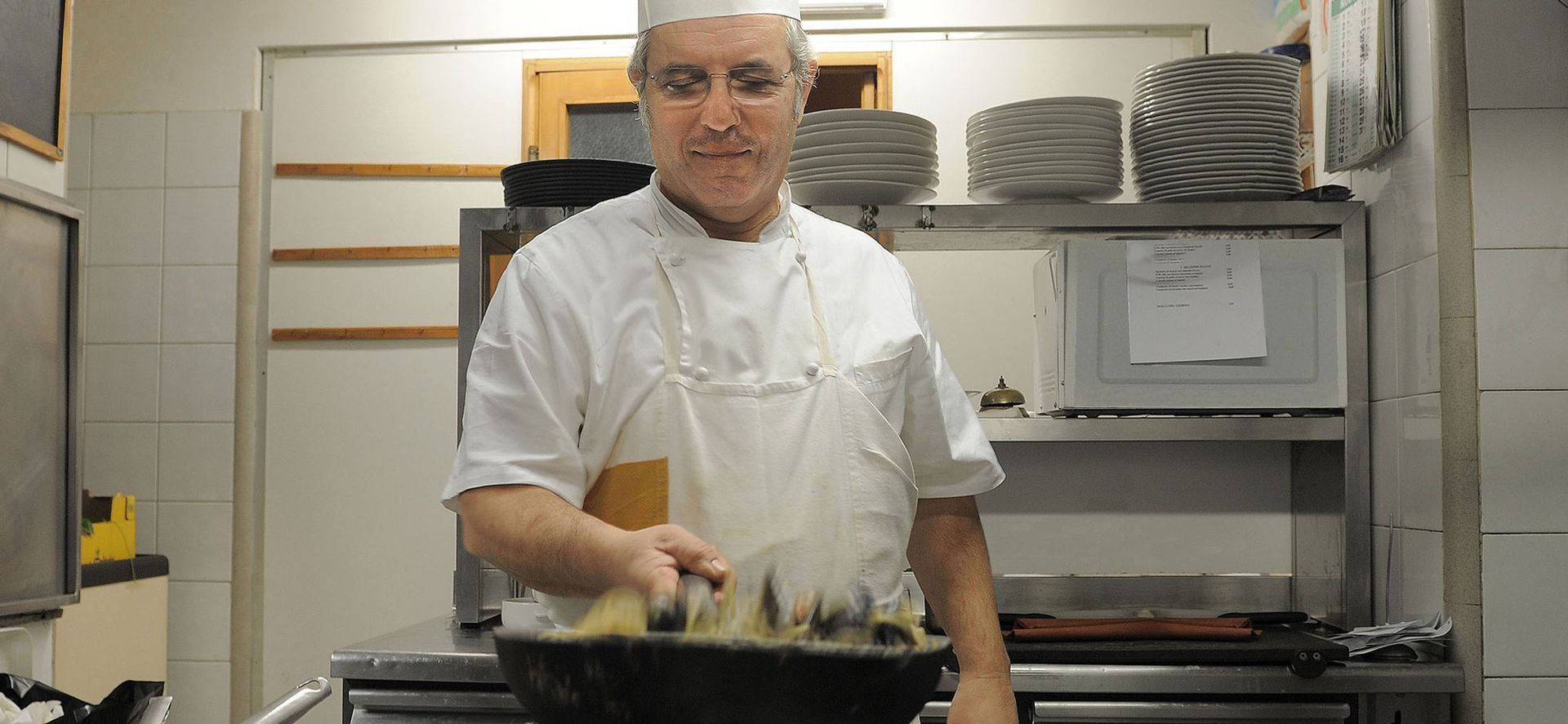 Cuoco in uniforme bianca che mescola il cibo in una grande pentola in cucina.