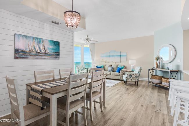 A bright, coastal-style dining room opens to a living area with ocean views, featuring light wood floors and soft decor.
