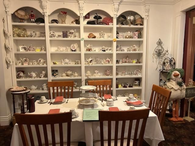 A dining room with a table and chairs and shelves filled with tea cups and saucers