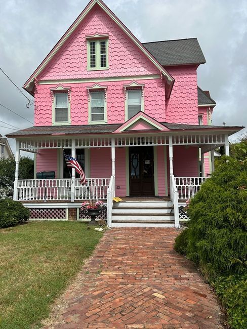 A pink house with a porch and a brick walkway.
