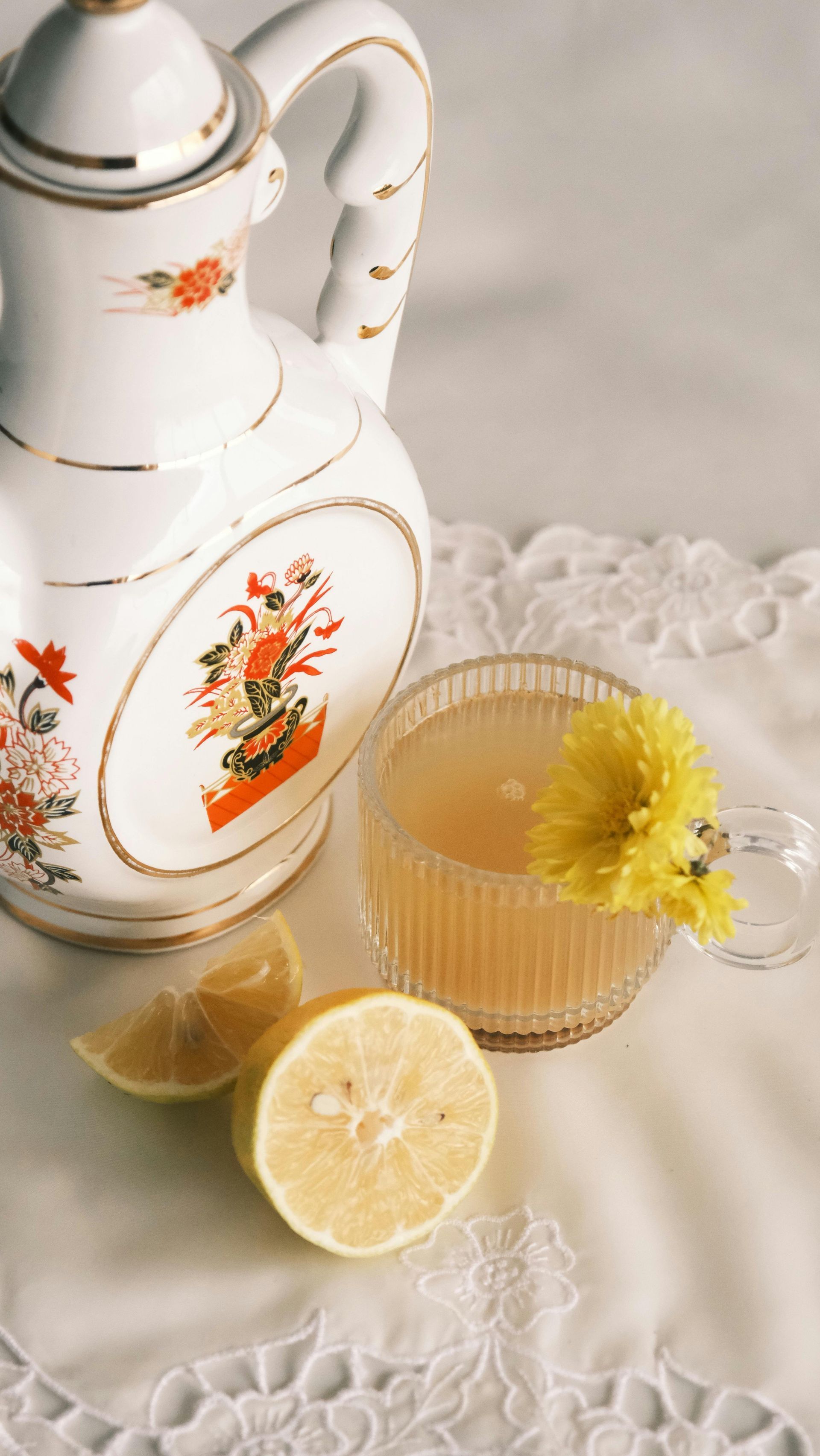 A teapot, cup of tea, lemon slices and a flower on a table.