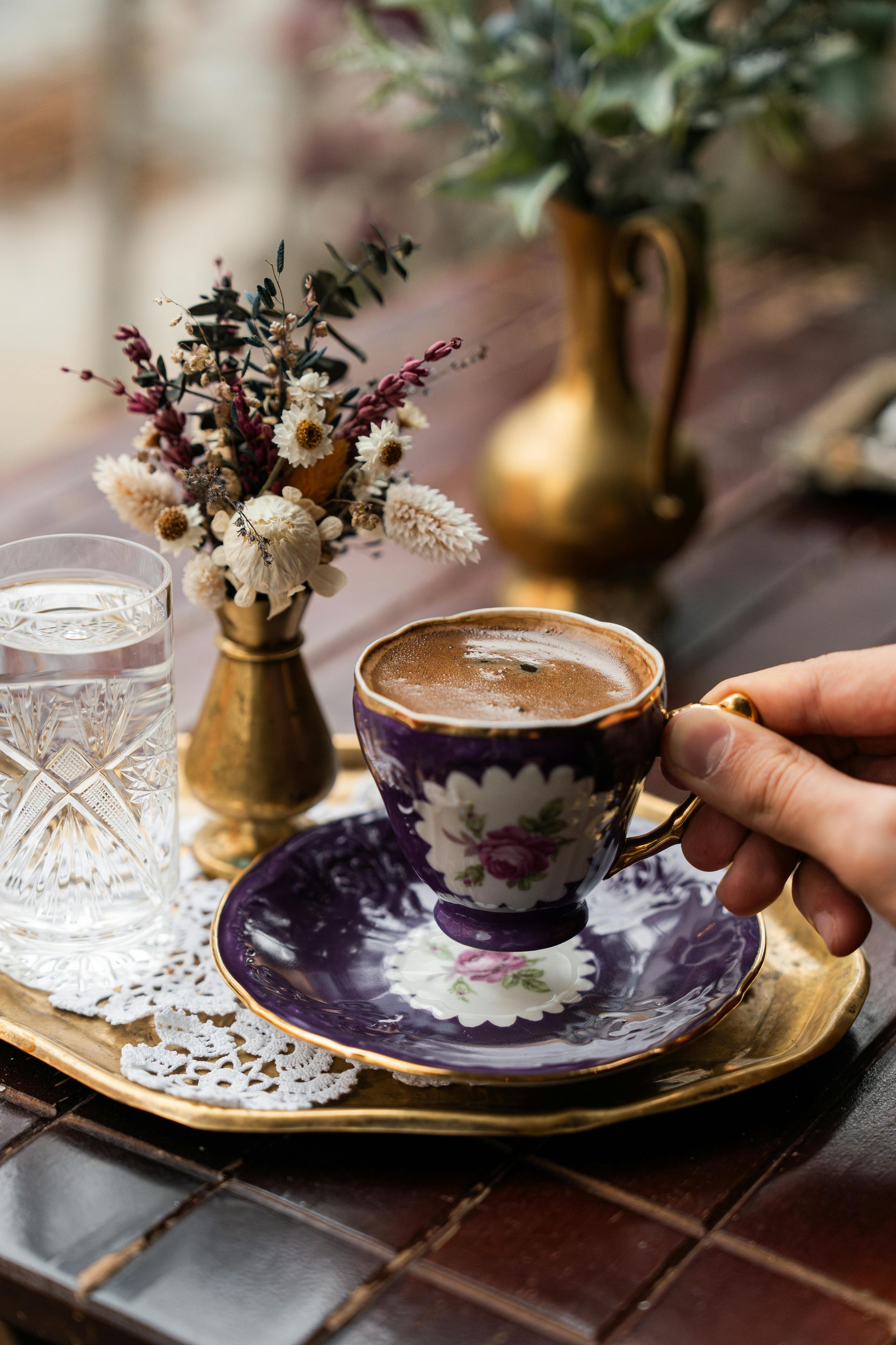 A person is holding a cup of coffee on a saucer on a tray.