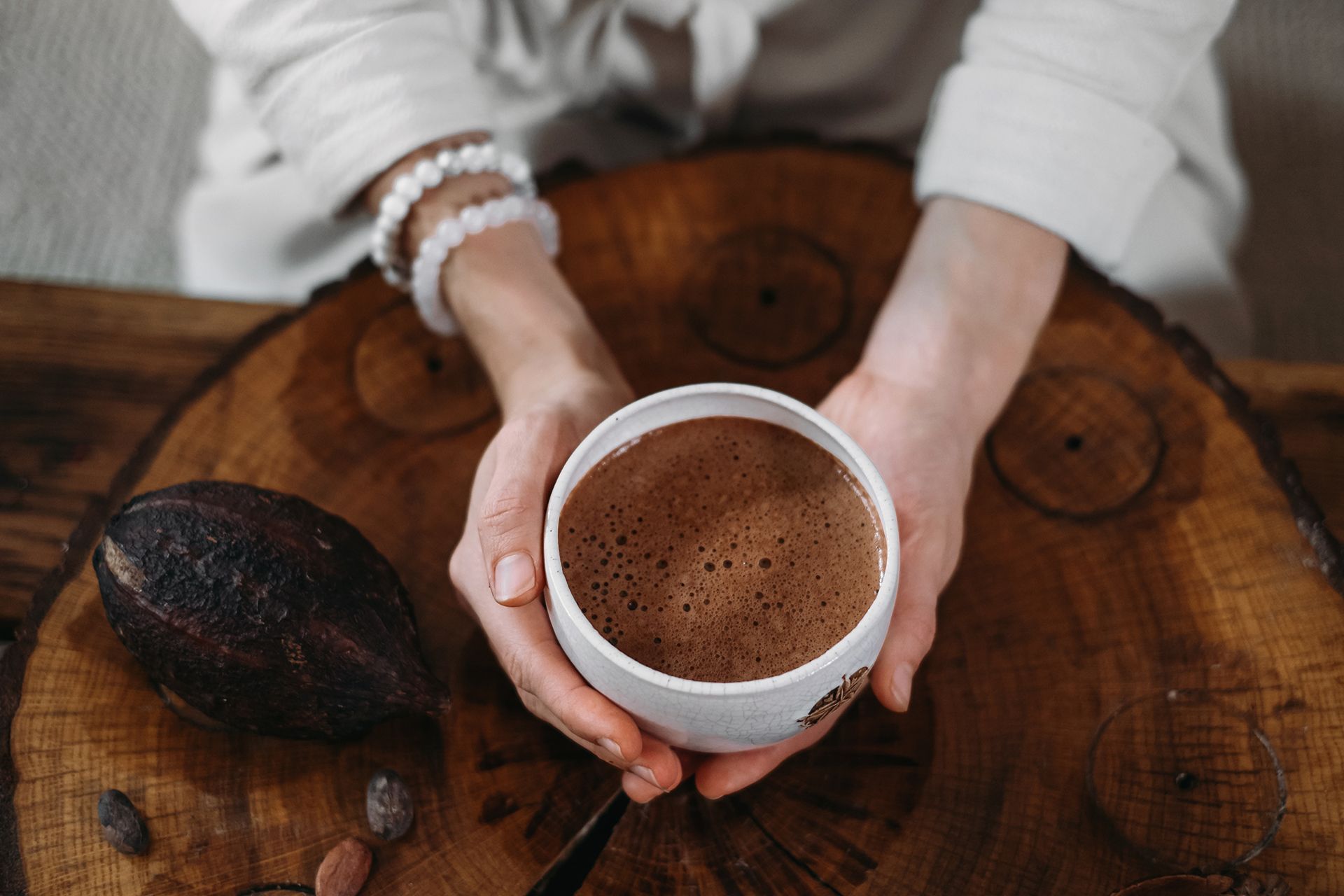 A woman is holding a cup of hot chocolate on a wooden table.