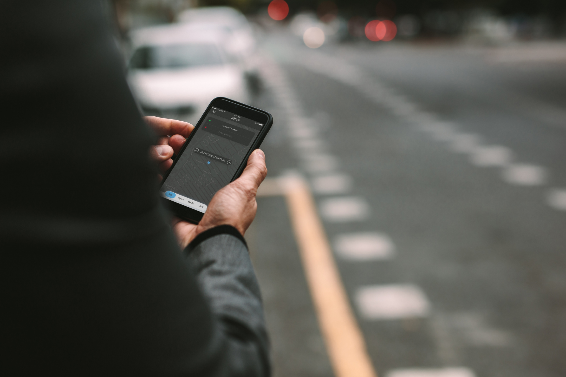 A person is holding a cell phone in their hand in front of a street.