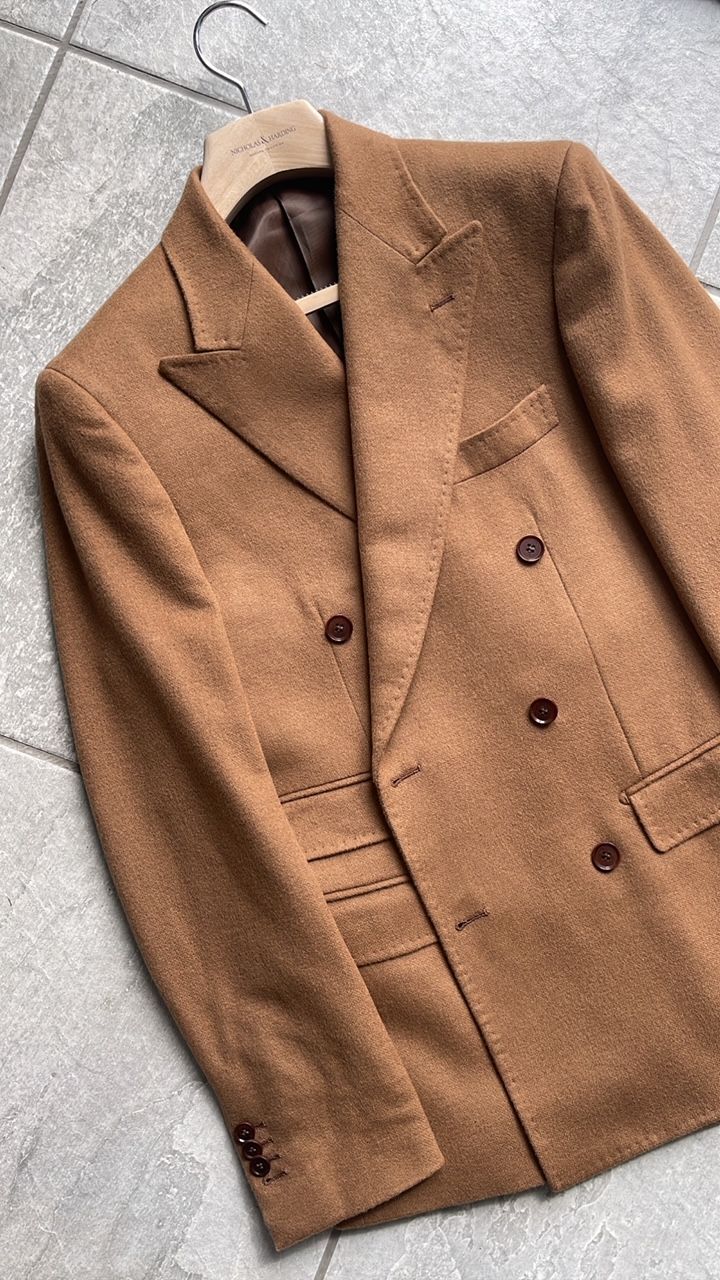 A brown suit jacket is hanging on a hanger on a tiled floor.