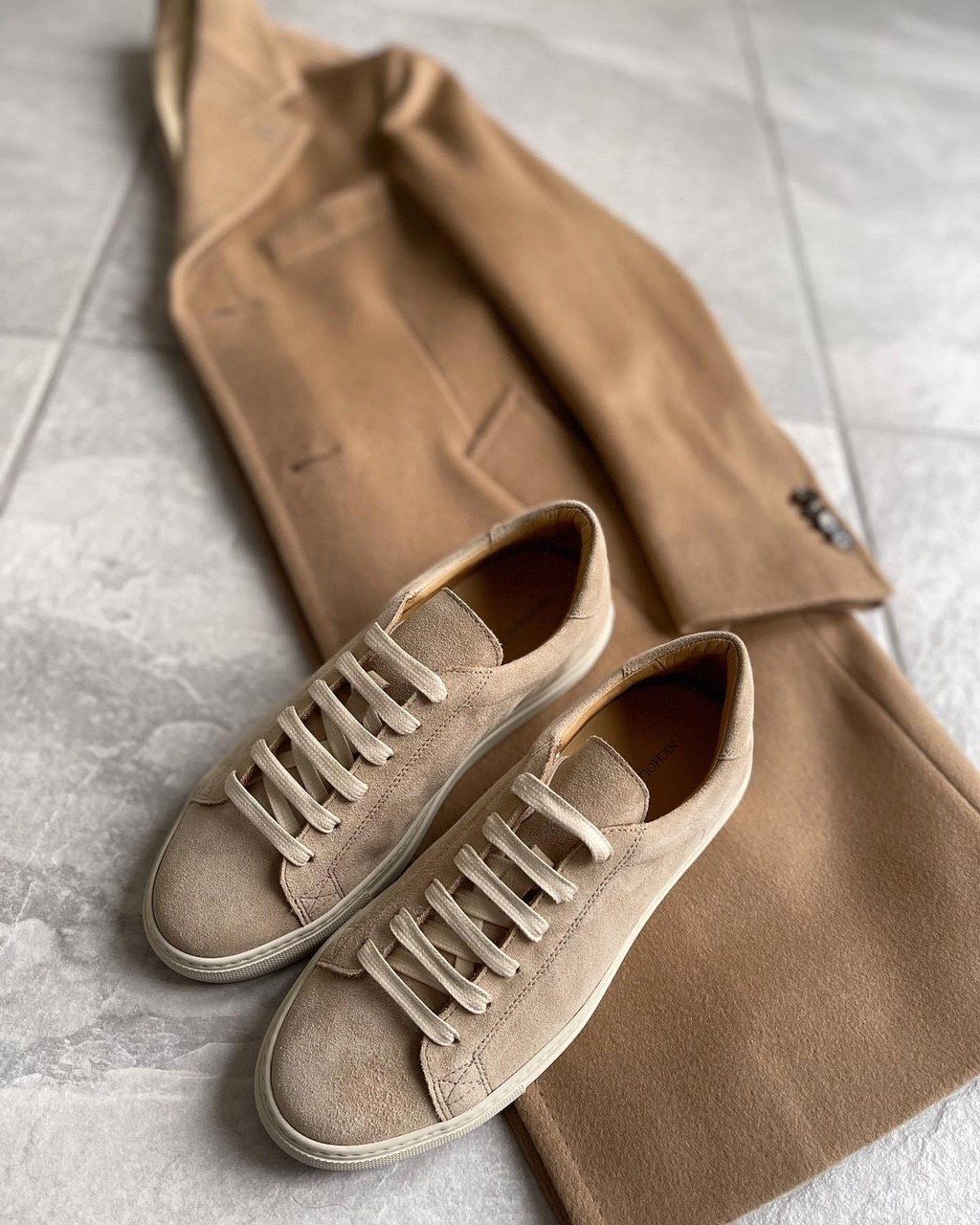 A pair of sneakers sitting on top of a camel coat.