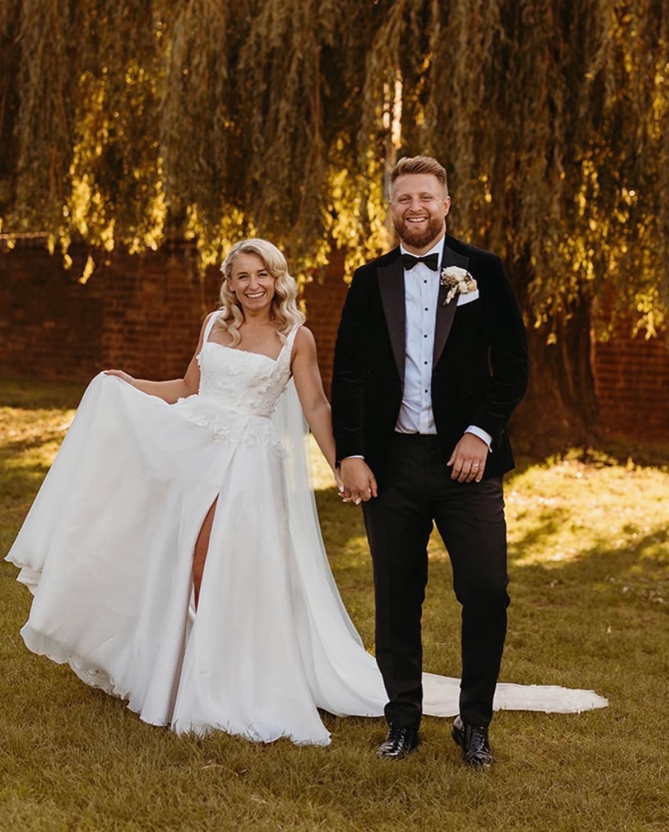 A bride and groom are standing next to each other in a field holding hands.