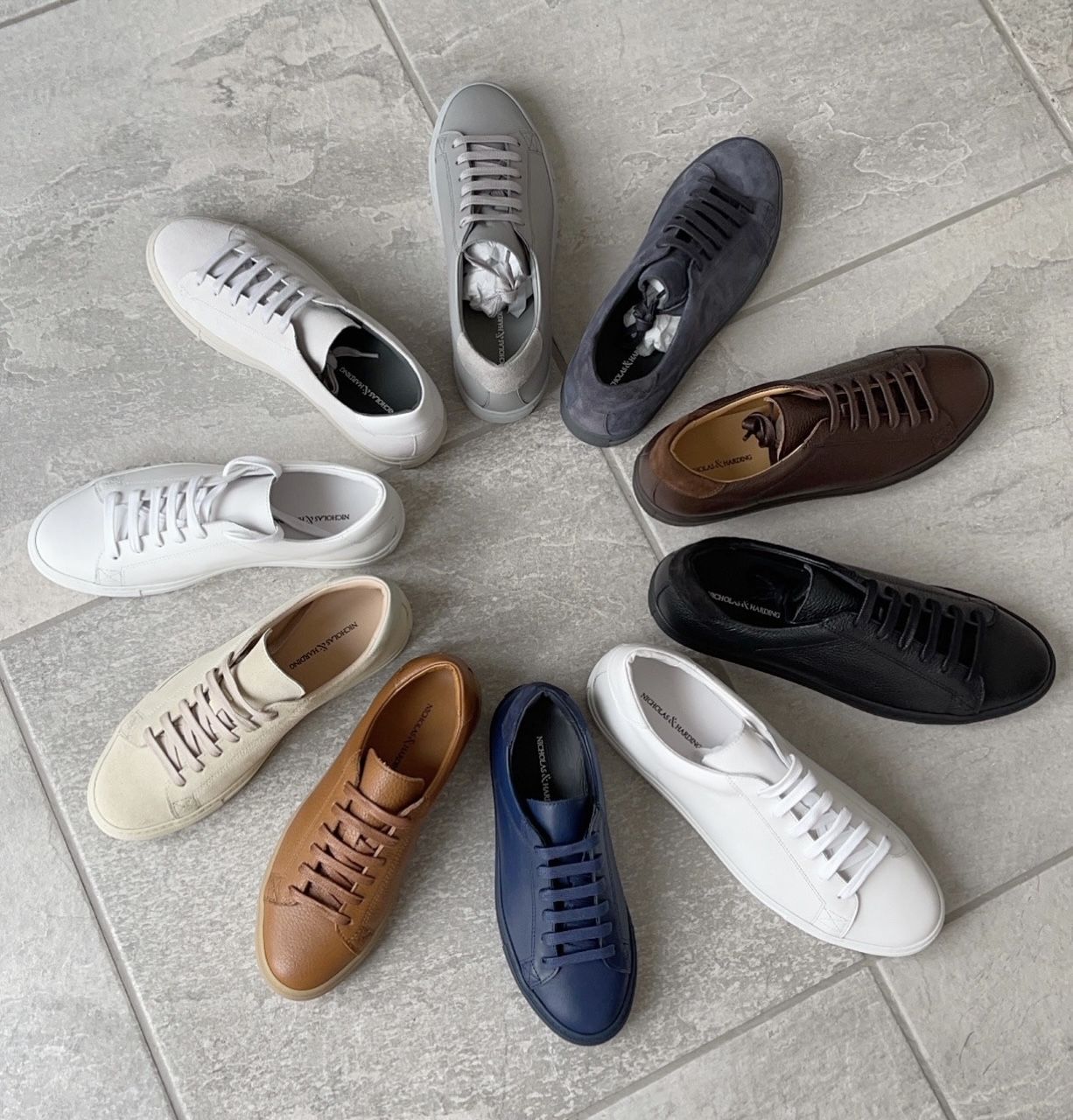 A variety of shoes are arranged in a circle on a tiled floor.