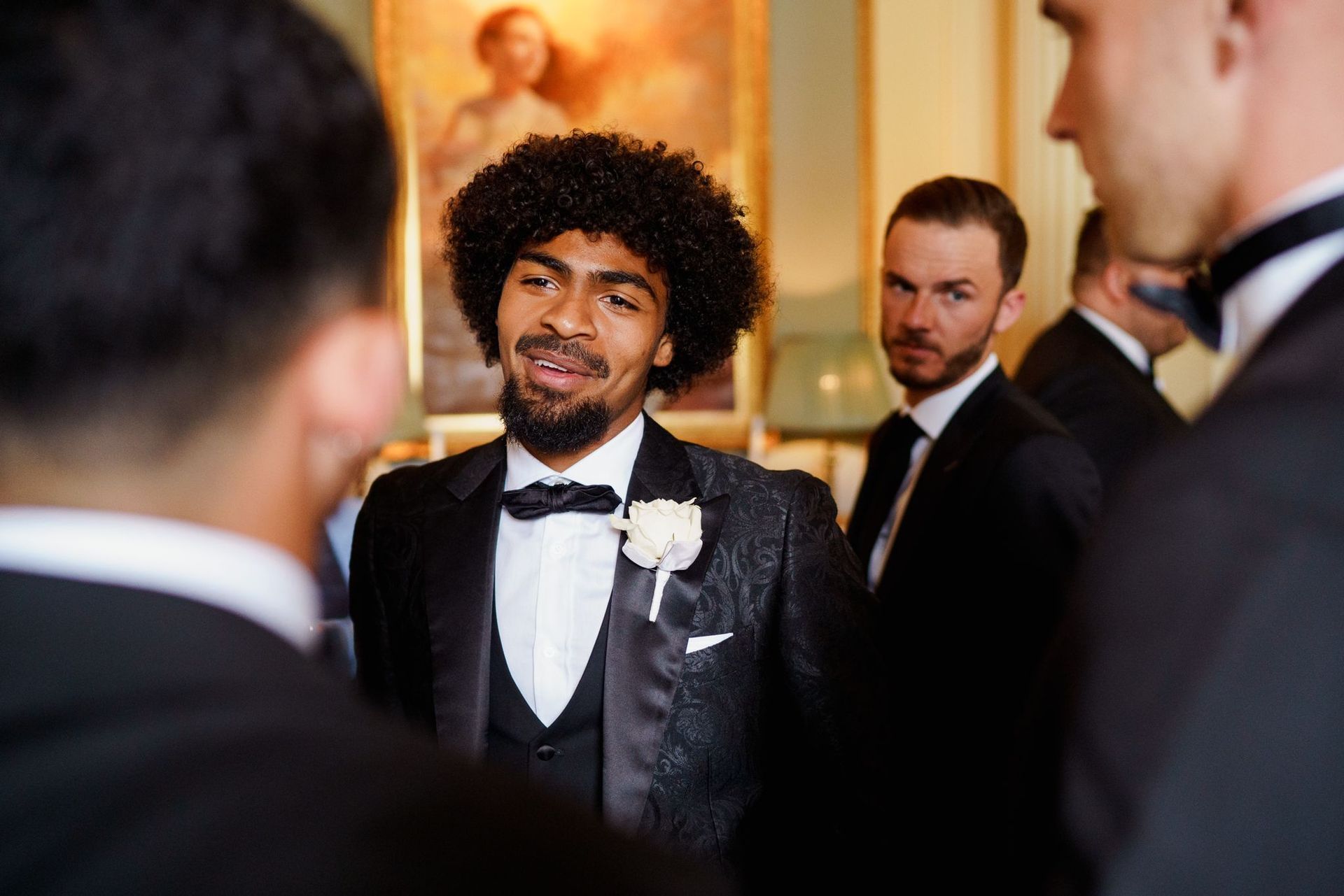 A man in a tuxedo is talking to a group of men.