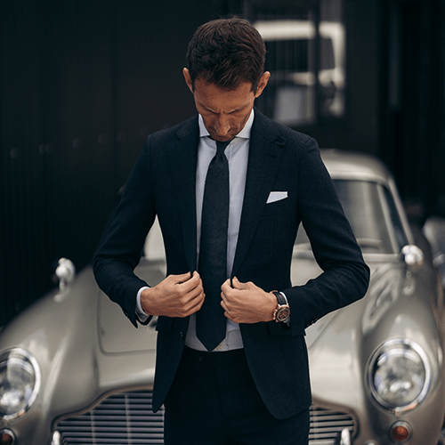 A man in a suit and tie is standing in front of a car.