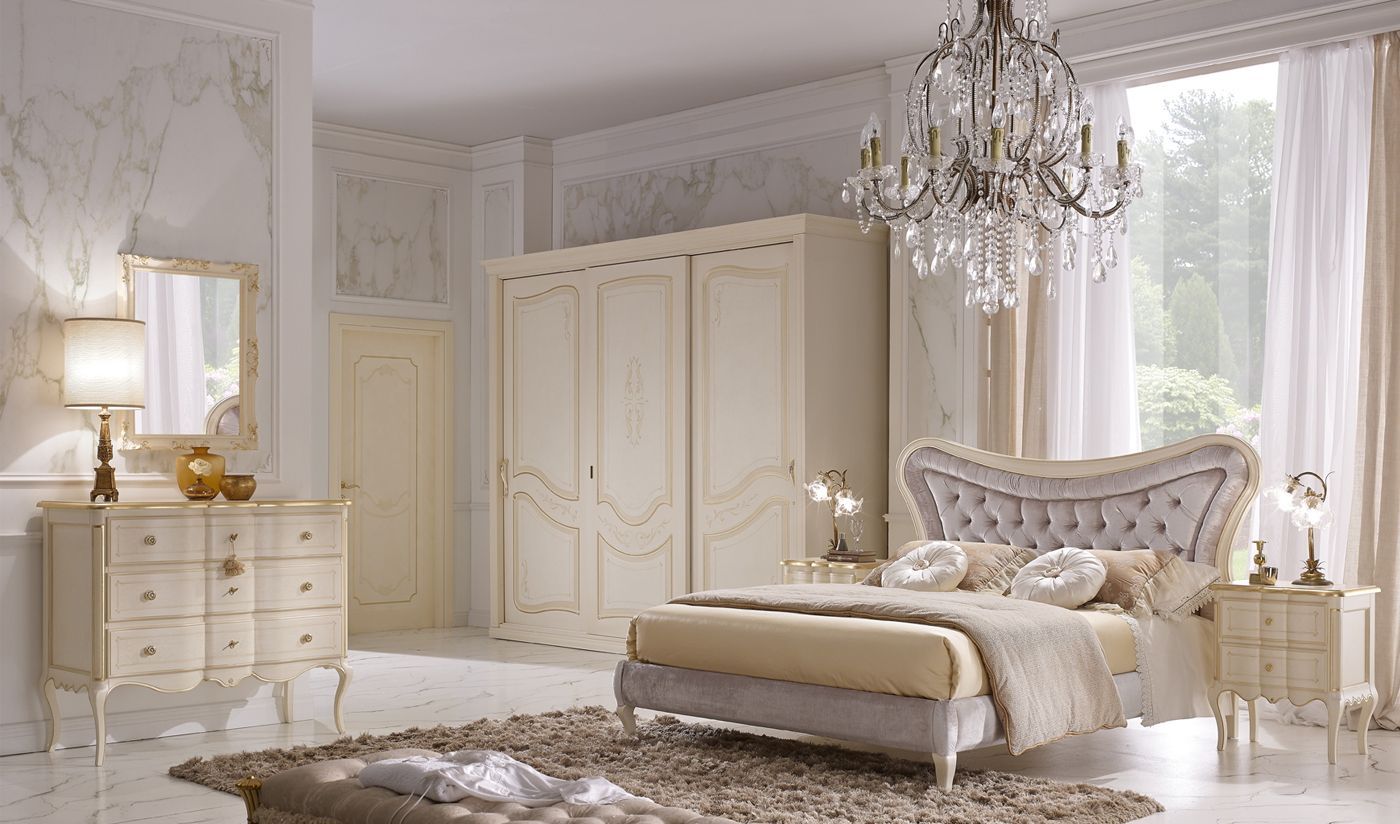 Elegante camera da letto con mobili color crema: letto, cassettiera, armadio. Lampadario, finestra con tende trasparenti.