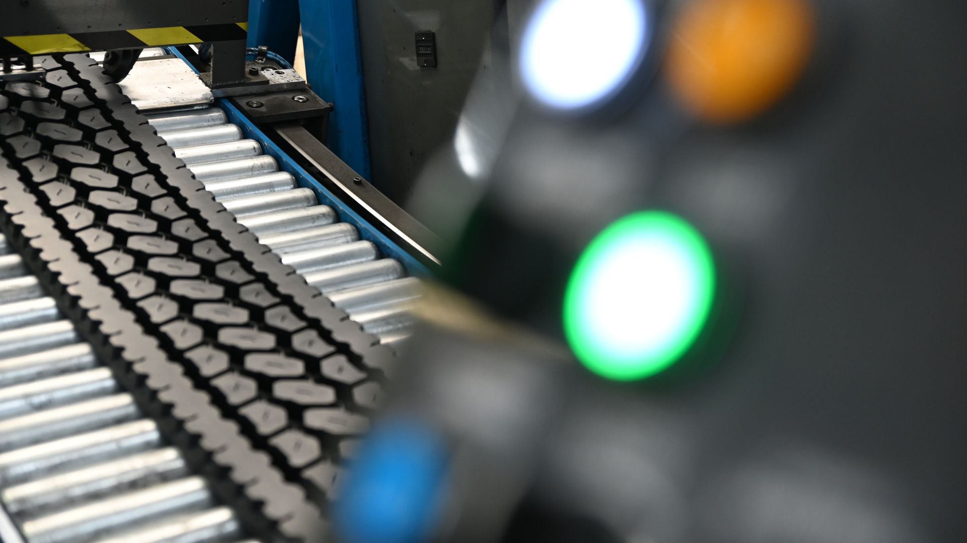 Tire tread on a conveyor belt; control panel with green, orange, and white lights in focus.