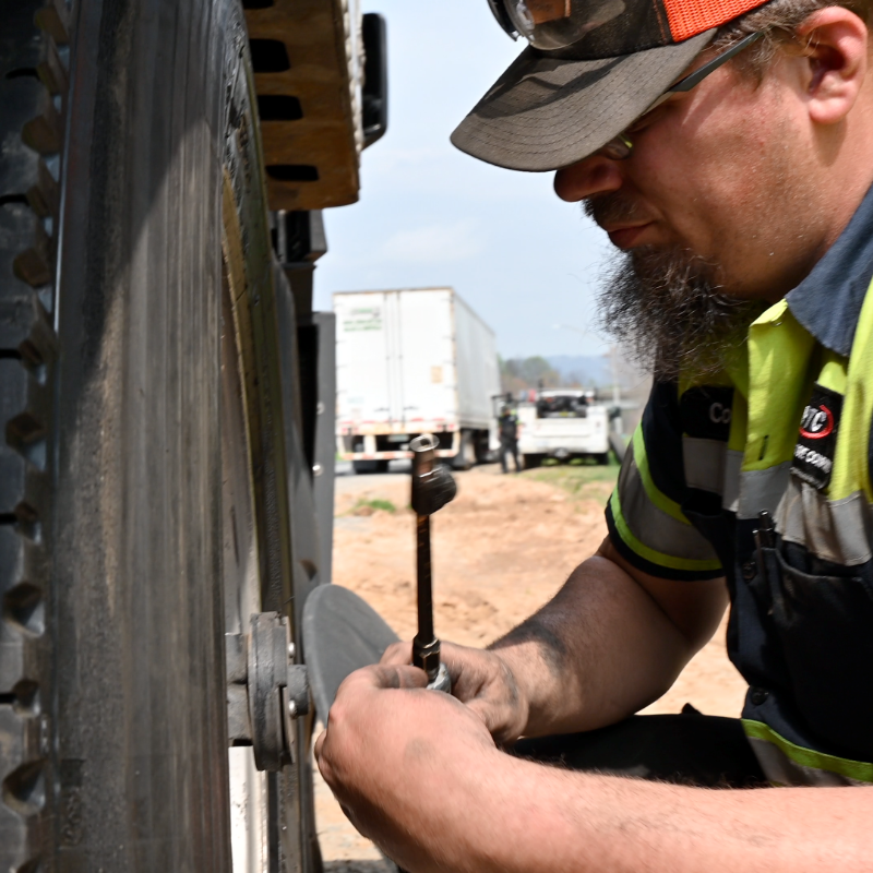 Mechanic fixing truck tire with grinder outdoors.