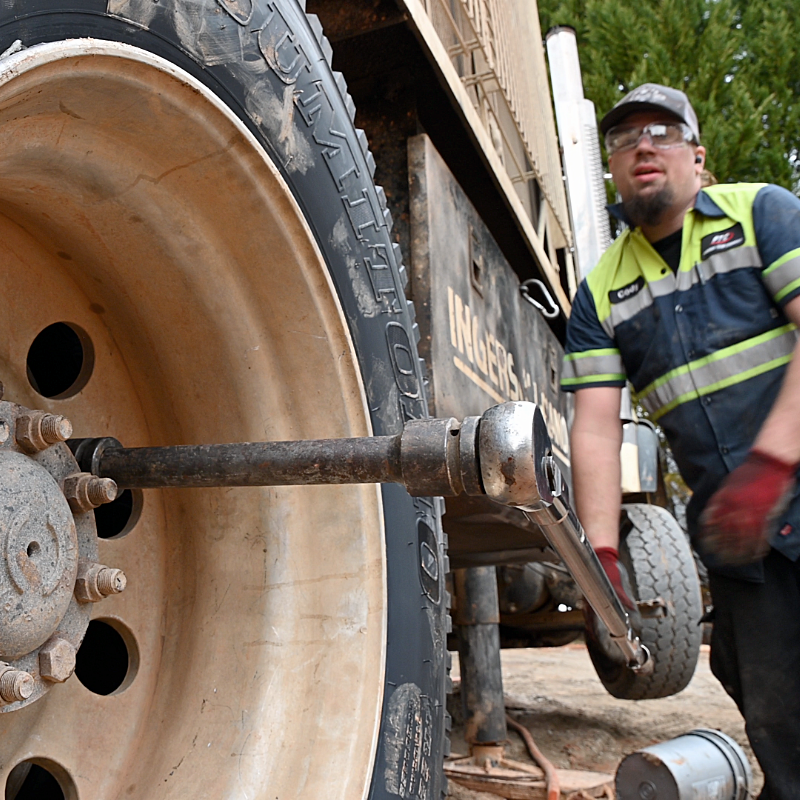 Mechanic using a wrench on a truck wheel outdoors.