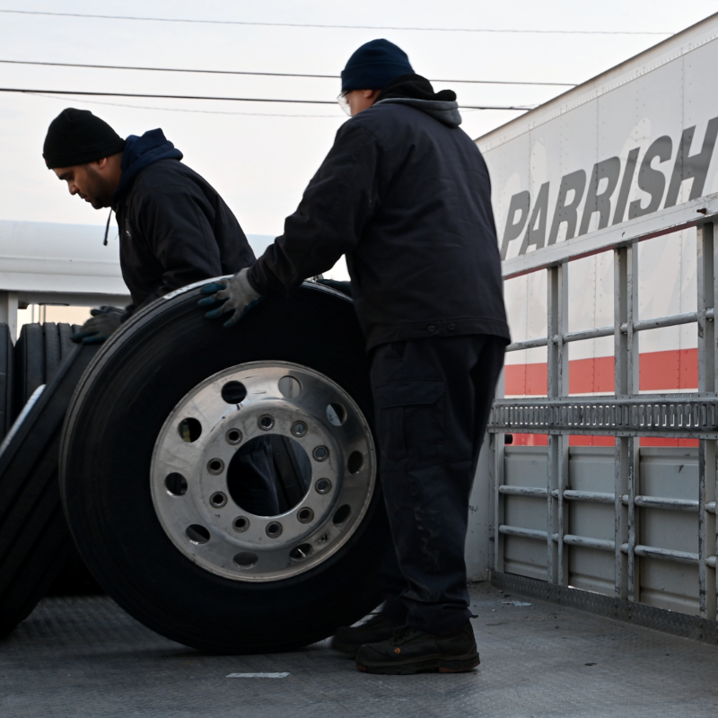 Two workers loading truck tires into a Parrish truck.