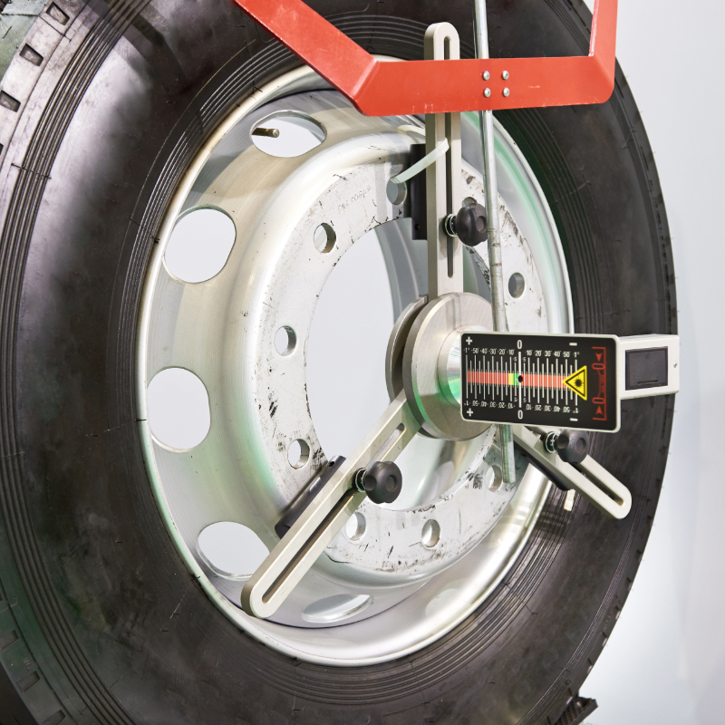 Wheel alignment equipment attached to a large truck tire, showing measurement display.