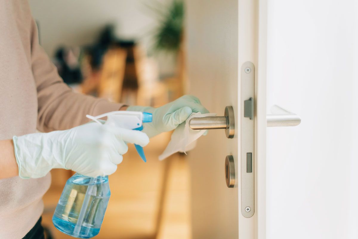 A person is cleaning a door handle with a spray bottle and a cloth.