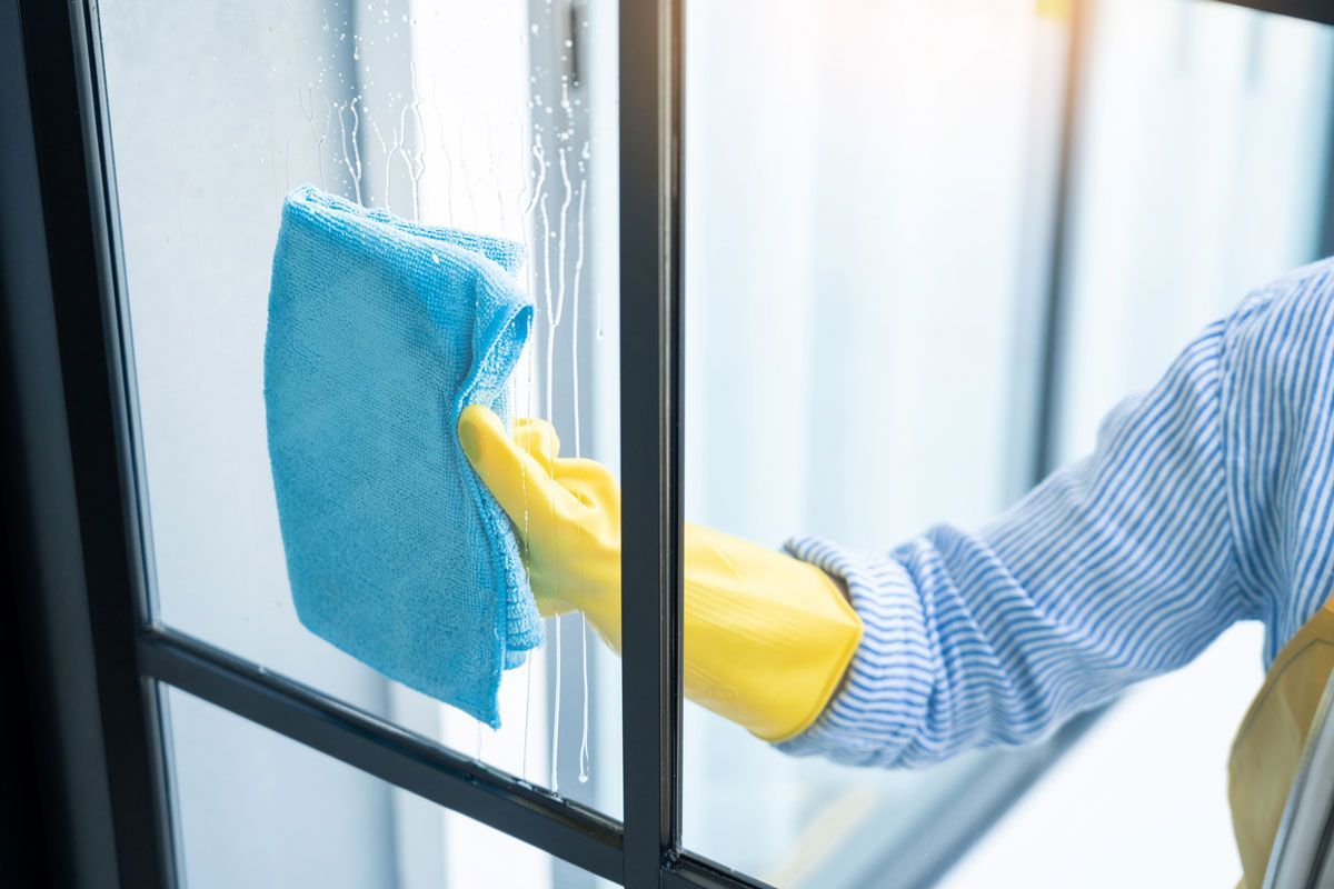 A person wearing yellow gloves is cleaning a window with a blue cloth.