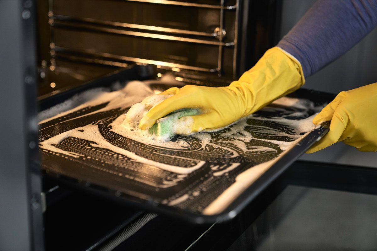 A person wearing yellow gloves is cleaning an oven with a sponge.