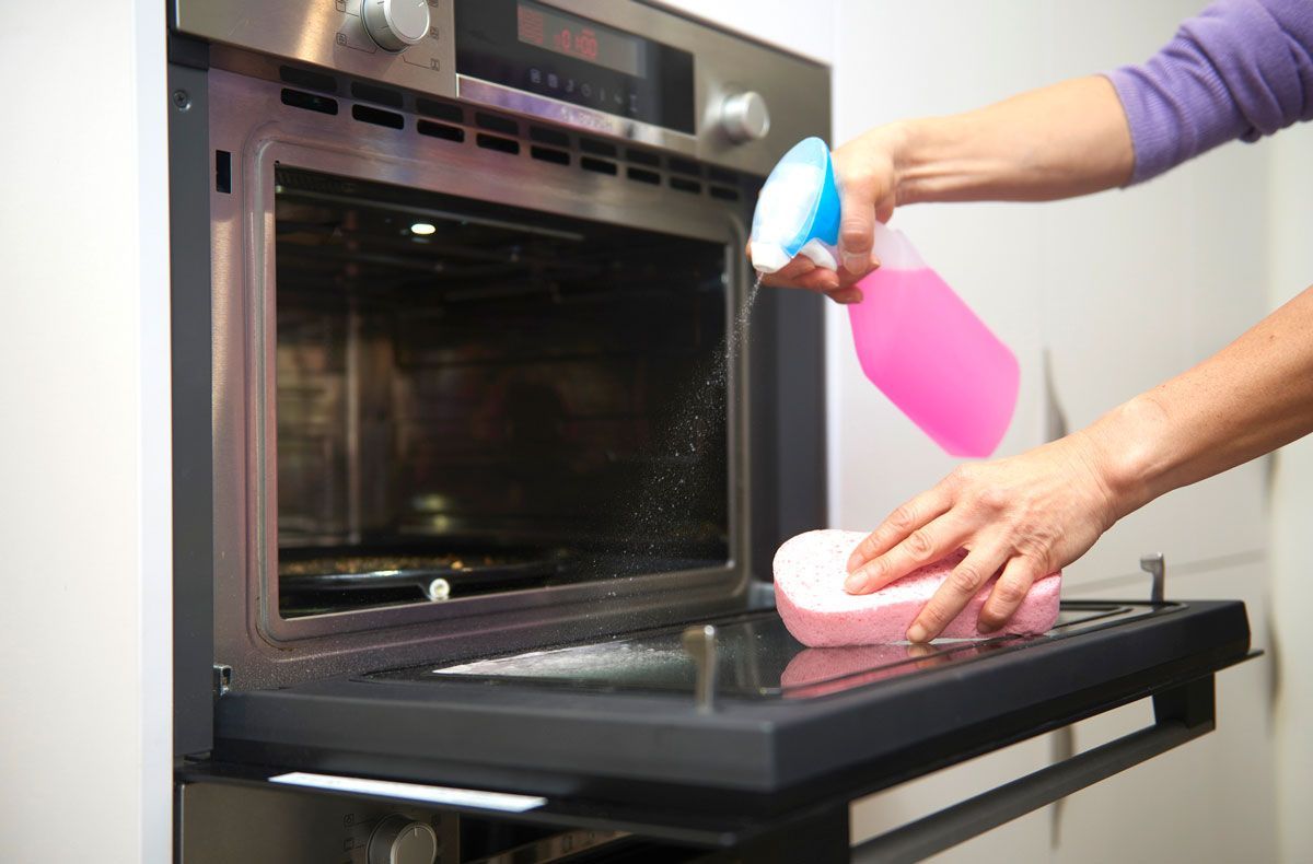 A person is cleaning an oven with a sponge and spray bottle.