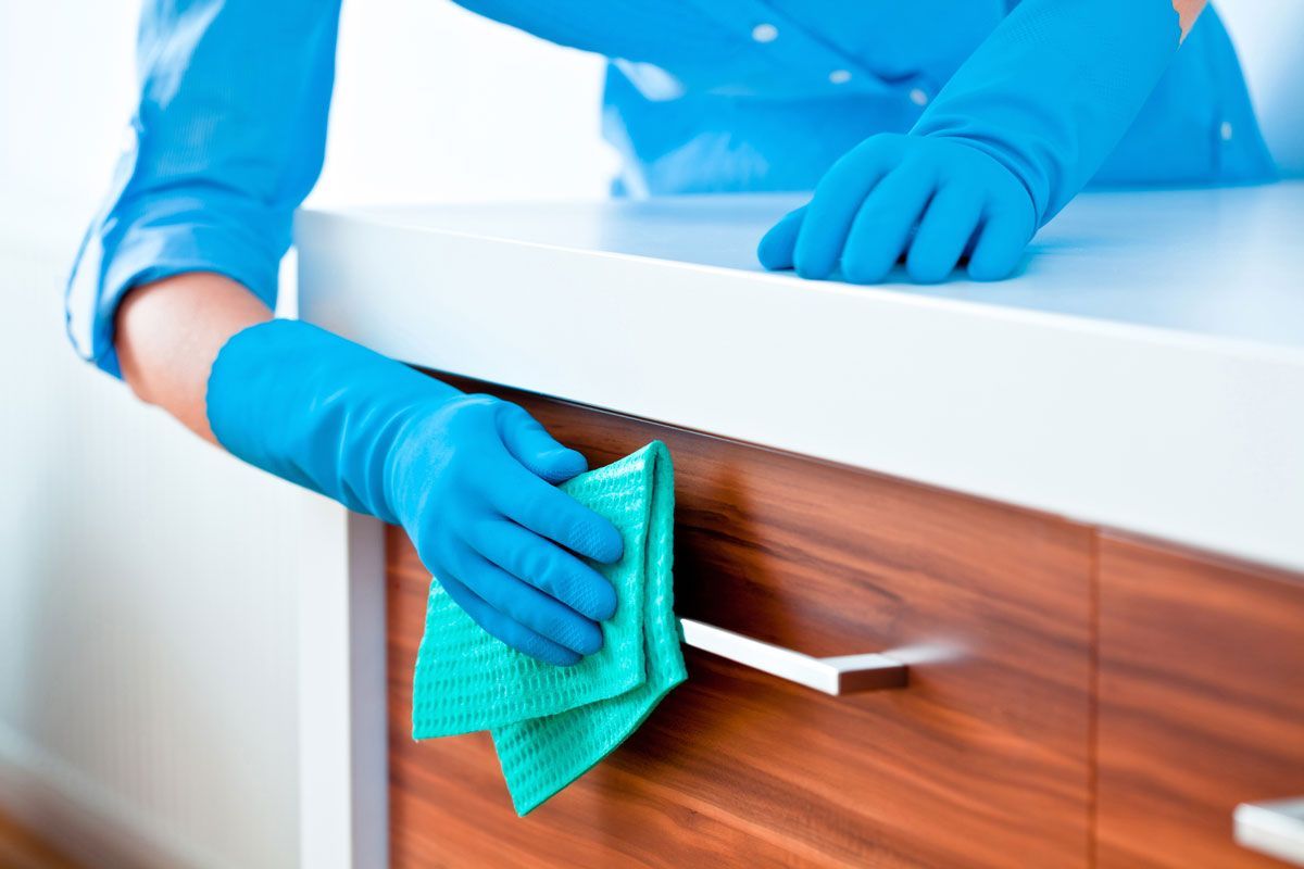 A person wearing blue gloves is cleaning a cabinet with a cloth.