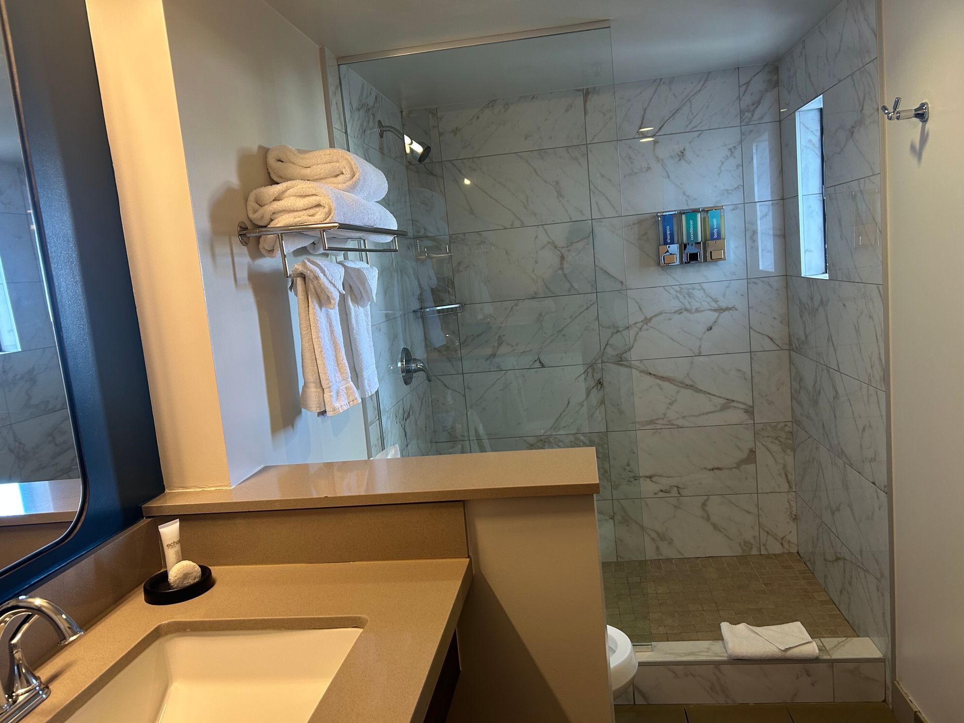 A bathroom with a sink , mirror and walk in shower.