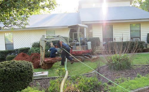 A man is digging a hole in the ground in front of a house.