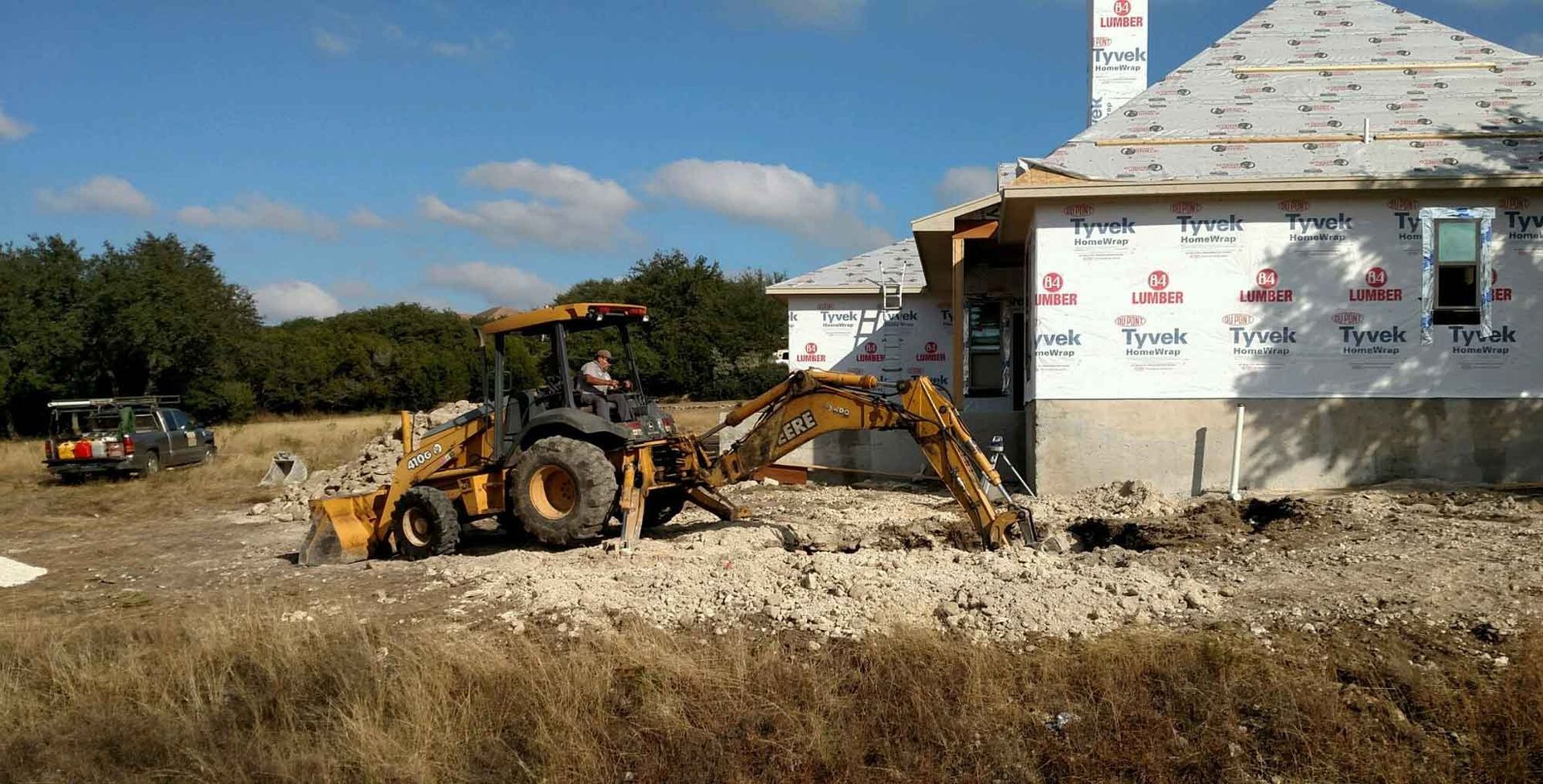 A man is driving a tractor in front of a house under construction