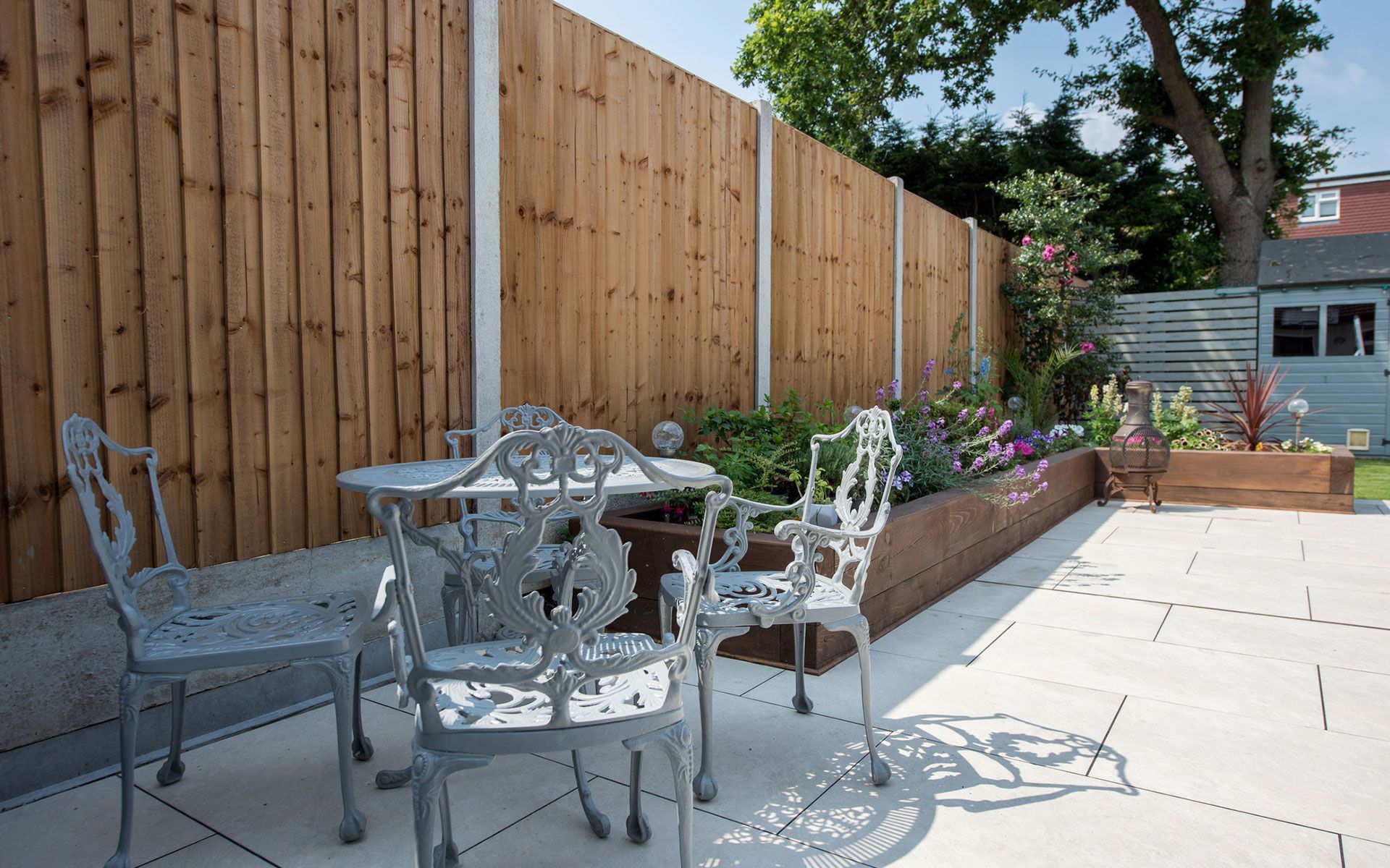 A wooden fence surrounds a patio with a table and chairs.