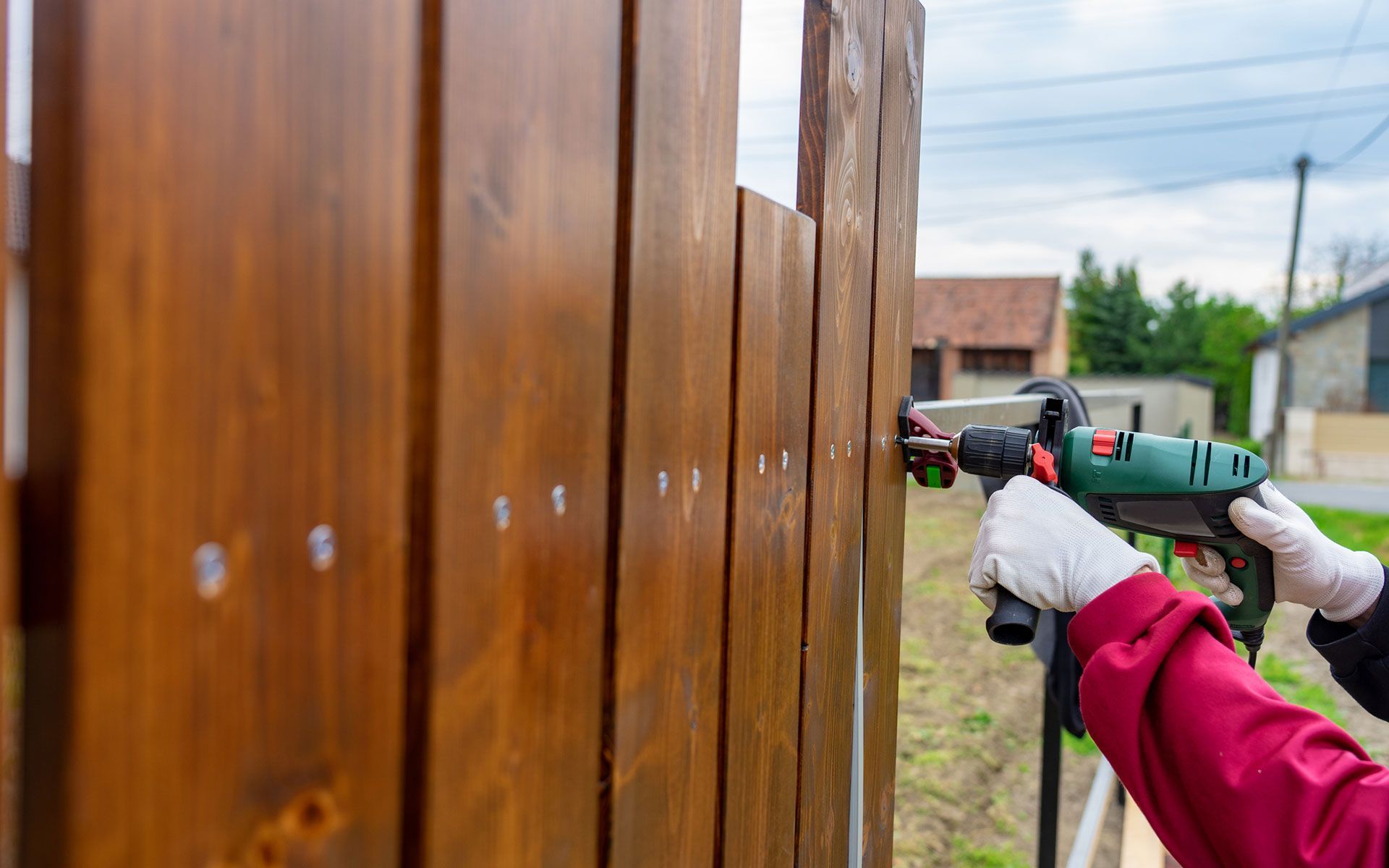 A person is using a drill to install a wooden fence.