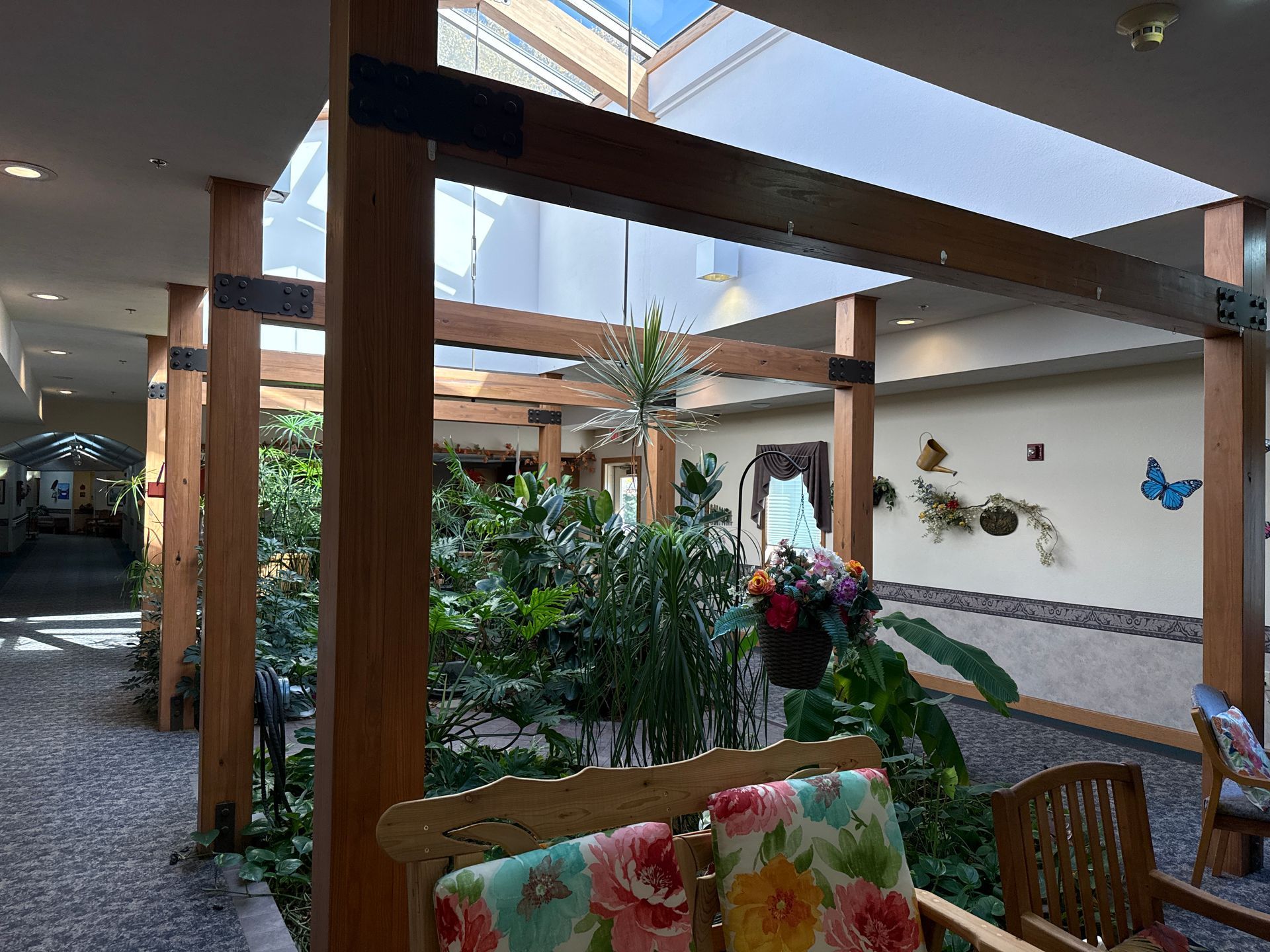 Indoor atrium with wooden beams, plants, and seating. Light streams through open roof.