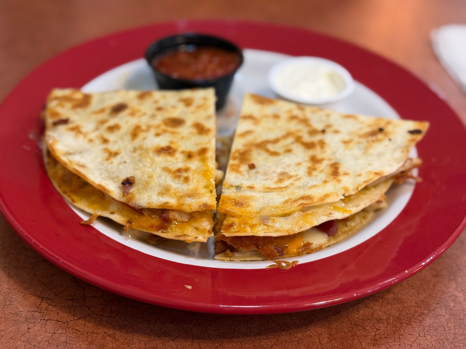 Quesadilla cut in half on a red-rimmed plate with salsa and sour cream.