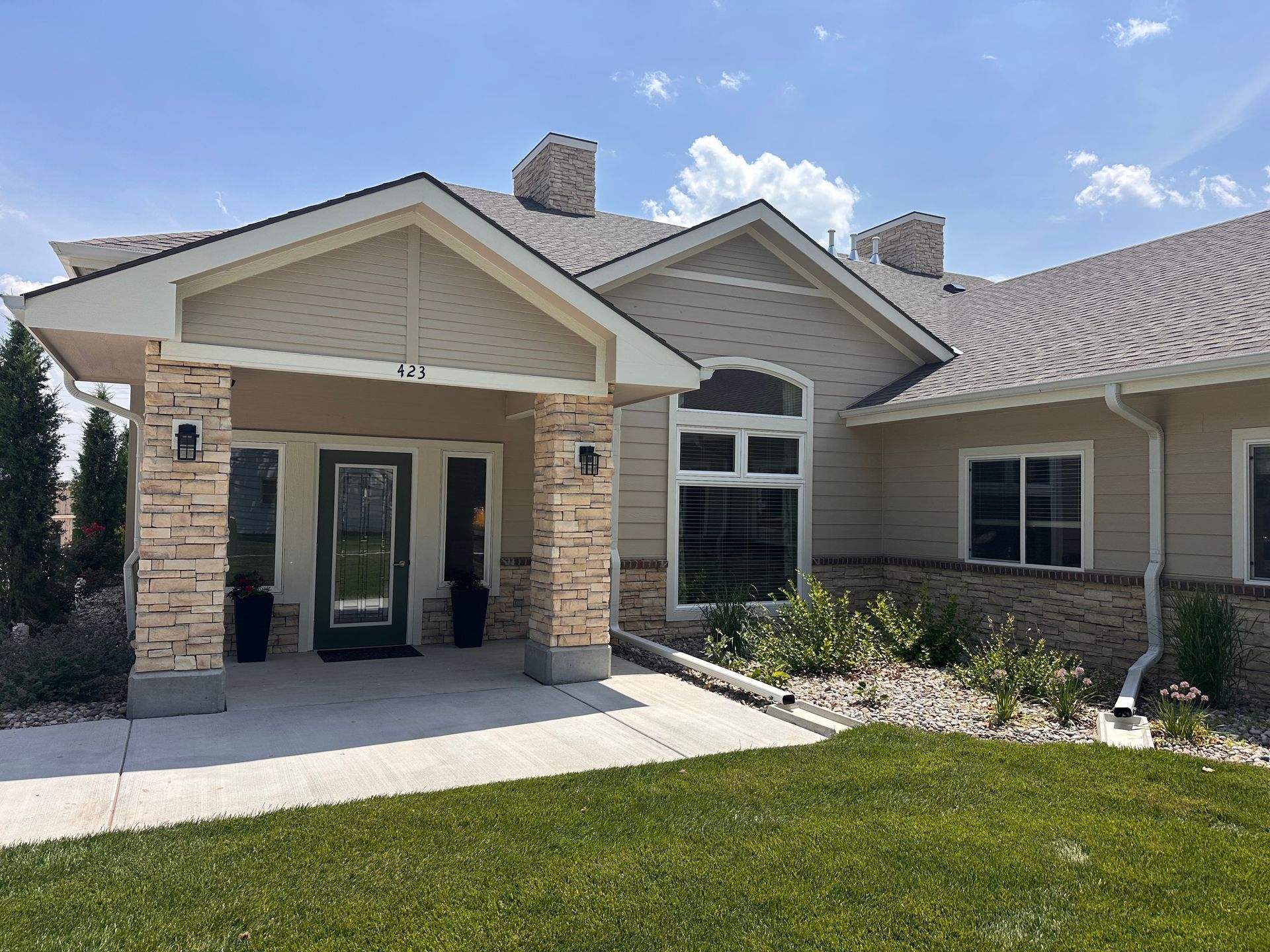 Beige building with stone accents, entrance with a covered walkway, and green grass.