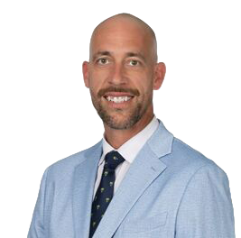 Bald man wearing a light blue blazer and patterned tie, smiling for the camera.