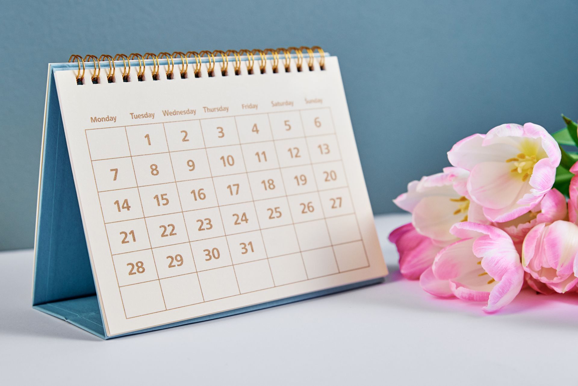 Calendar with open month dates and pink tulips next to it.