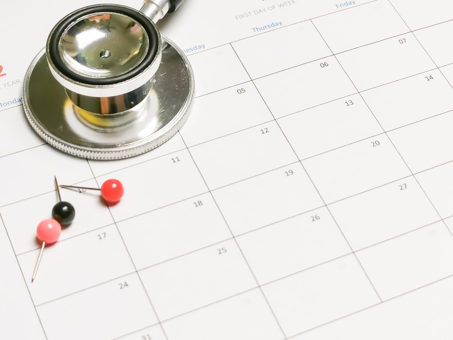 Stethoscope on a calendar, with pushpins. Medical appointment scheduling.