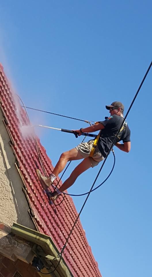 A man is cleaning the roof of a house with a high pressure washer