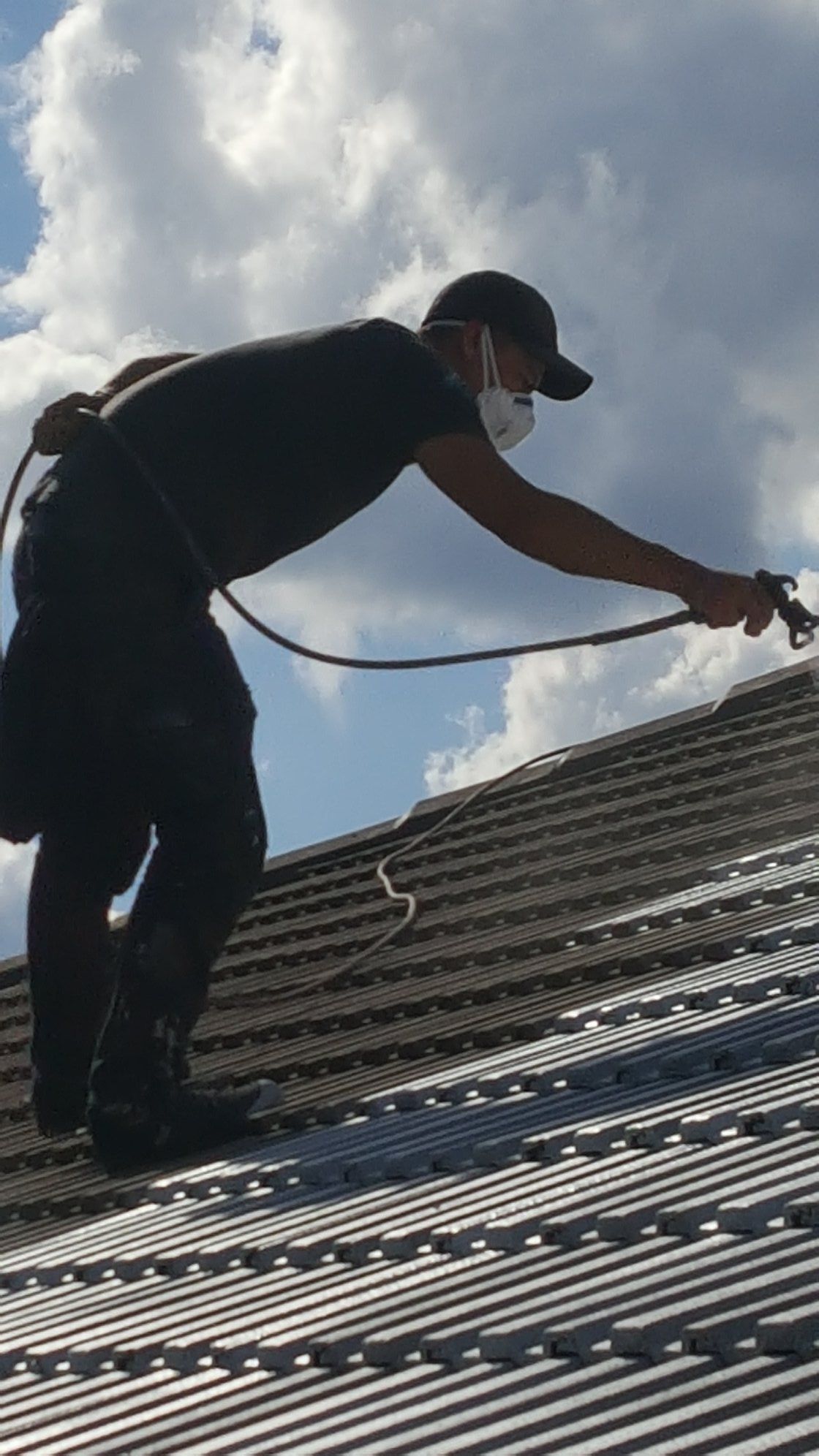 A man wearing a mask is spraying a roof with a sprayer.