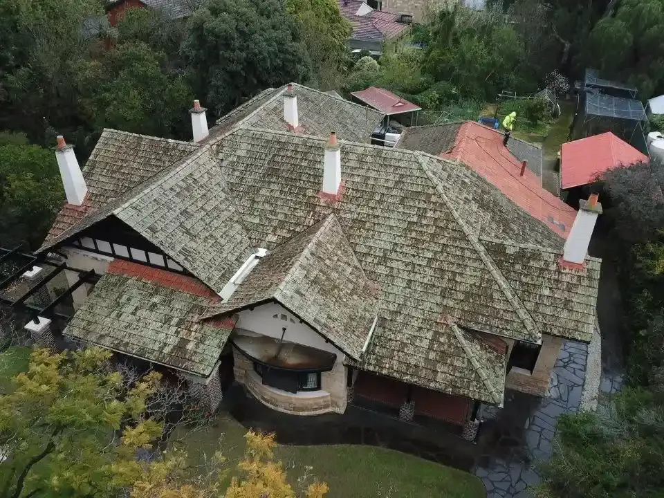 An aerial view of a large house with a tiled roof surrounded by trees.
