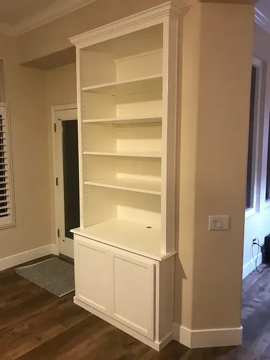 A white bookshelf is sitting in a living room next to a window.