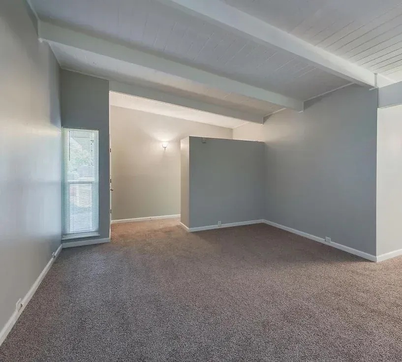 An empty living room with gray walls and a brown carpet.