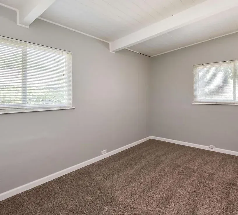An empty room with a carpeted floor and two windows.