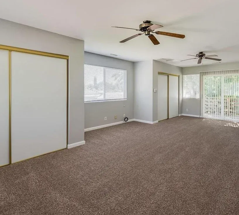 An empty living room with a ceiling fan and sliding glass doors