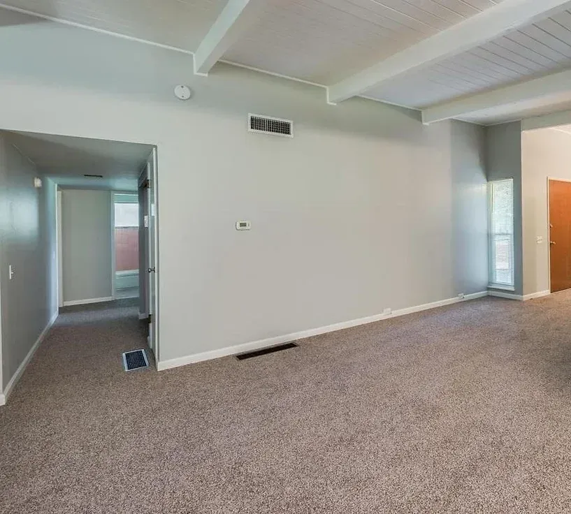 An empty living room with a carpeted floor and a ceiling fan.